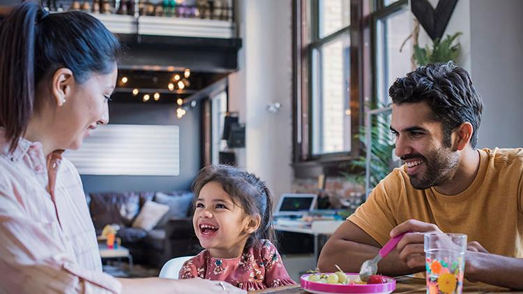 A mother and father sit at the table feeding their young daughter.