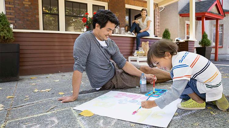 Child painting on the driveway with Dad while Mom watches from the front porch.