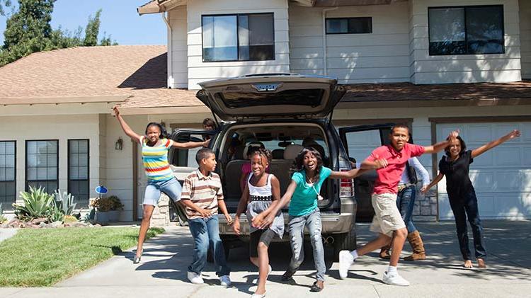 Six children are jumping with excitement outside in front of an SUV with the back hatch open.